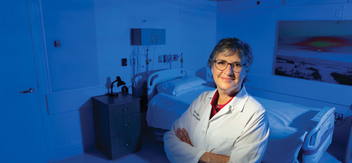 Elizabeth Klerman in white lab coat with arms crossed with bed in back of her.