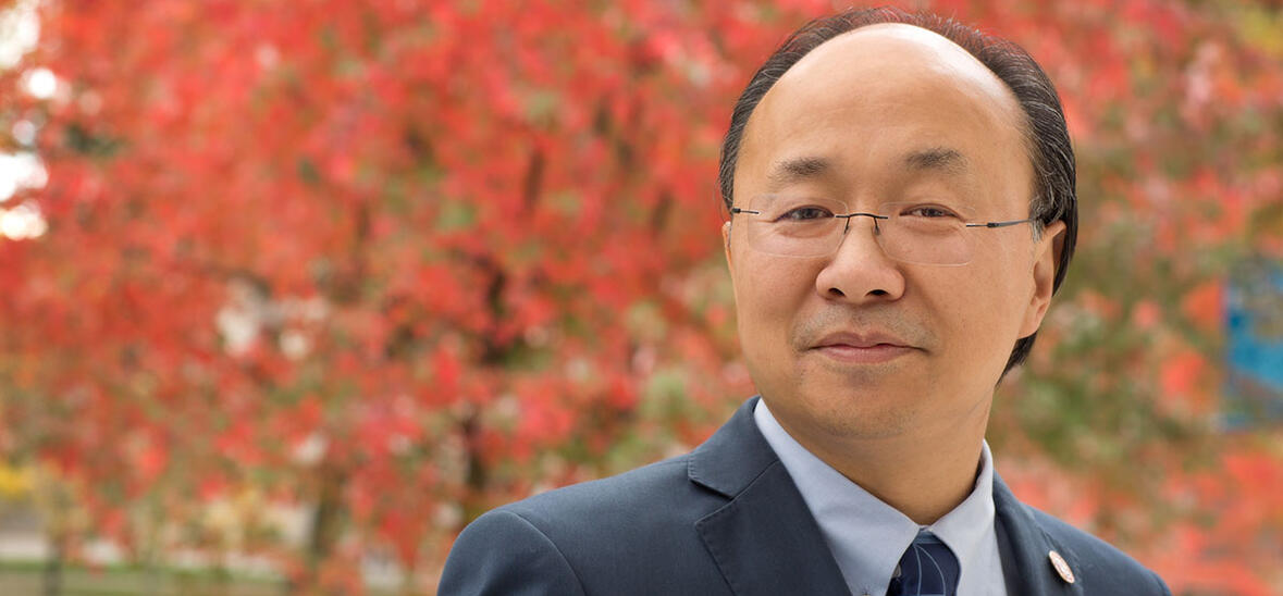 Professor Xiao-Li Meng in front of tree with red leaves