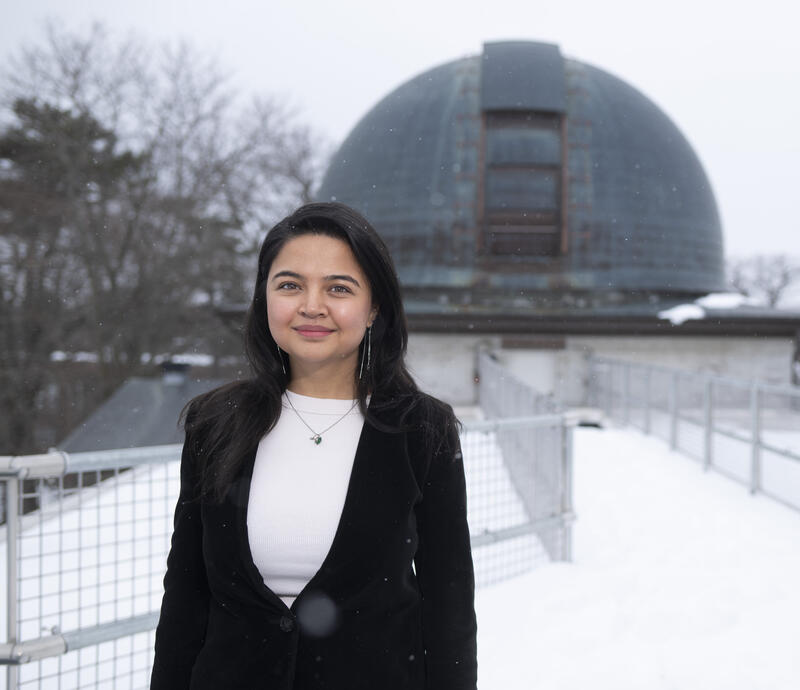 Student smiling in front of the Harvard–Smithsonian Center for Astrophysics dome on a snowy day