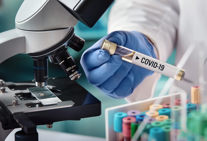 COVID-19 vial being held in lab next to microscope