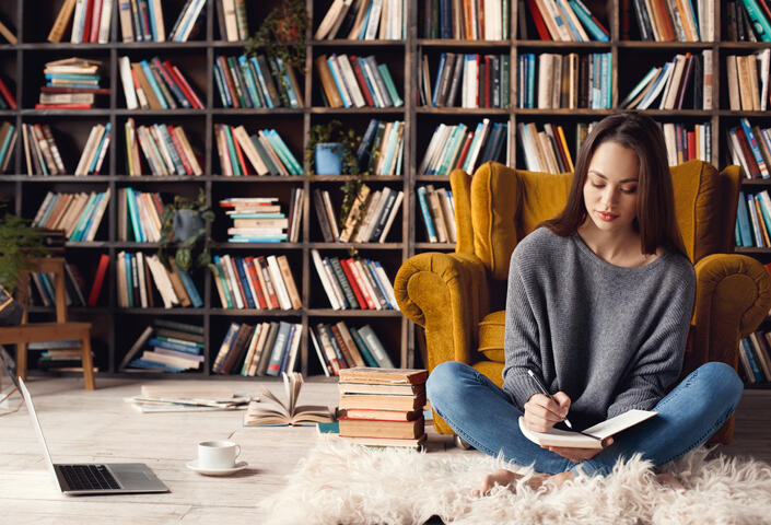 Woman sitting on floor with book in hand and bookshelves behind her