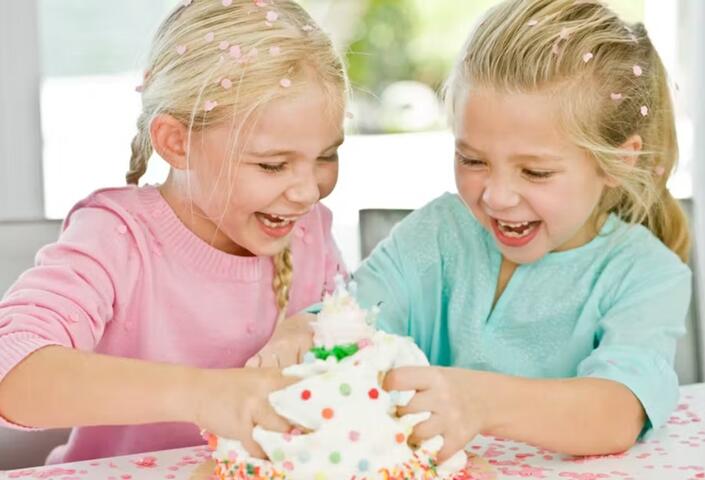 Photo of laughing girls dividing up a cake with their bare hands 