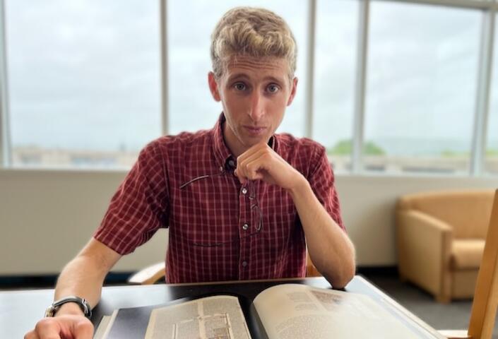 Headshot of Daniel Jacobs; hand on chin with book on desk