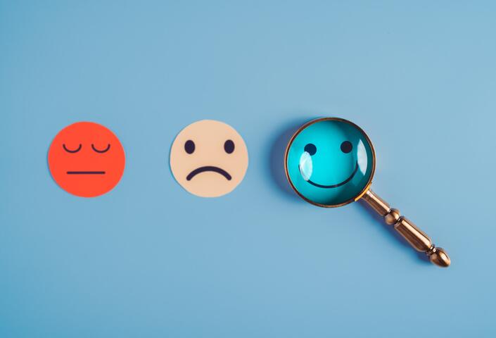smiling face, frowning face, neutral face, with magnifying glass over smiling face