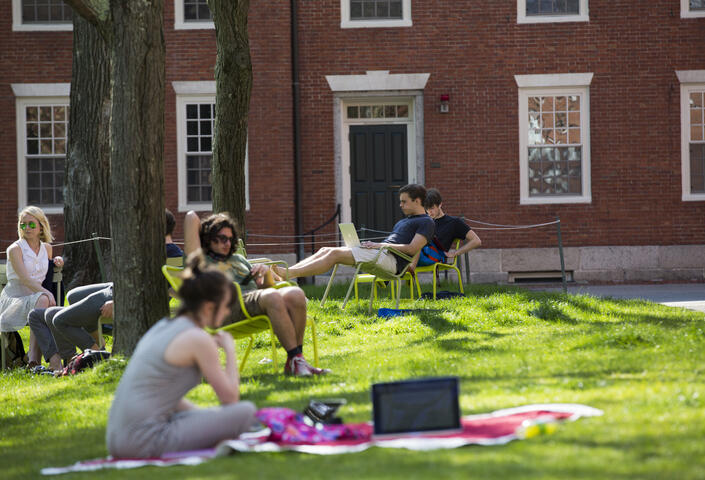 People sitting down on grass and in chairs in Harvard Yard