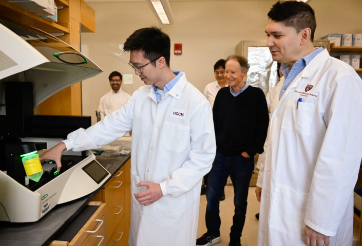Dr. Bruce Yankner (center) watched as Zhen Kai Ngian (left) described the role of a digital droplet PCR machine used in the team's Alzheimer's research at the lab in the Harvard Medical research building.