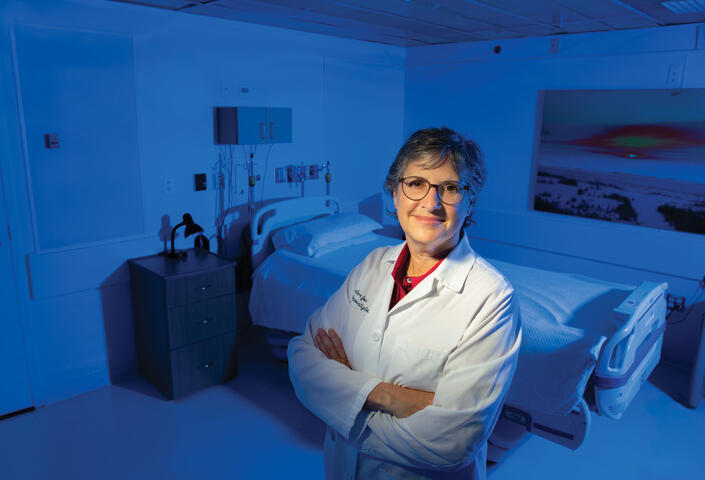 Elizabeth Klerman in white lab coat with arms crossed with bed in back of her.