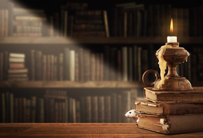 whimsical stack of books with candle melting on top and mouse peering out
