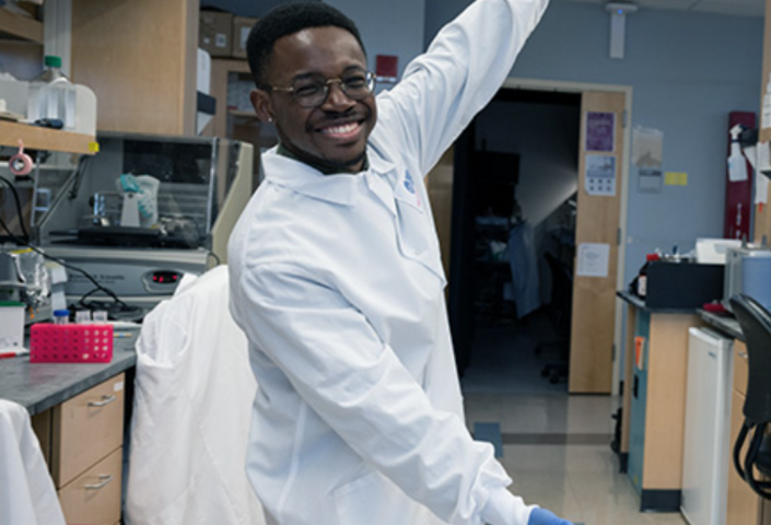 Olúmídé Fagboyegun smiling and gesturing toward his lab equipment
