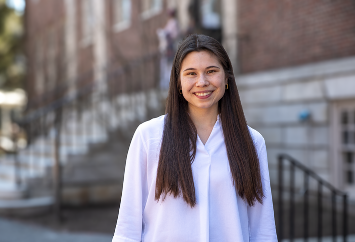 Abigail wearing a white shirt with hair down standing in front of Lehman Hall 