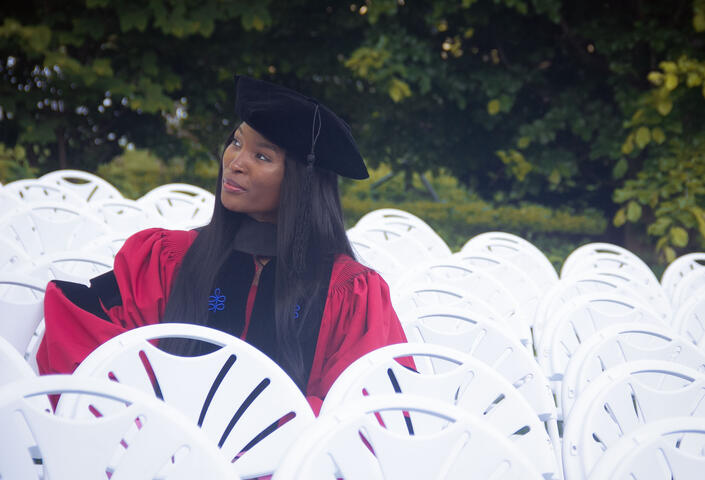 Nkem-Onyekpe sitting in a row of white chairs wearing regalia
