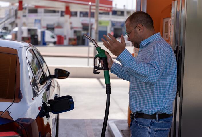 guy standing at gas pump seemingly frustrated