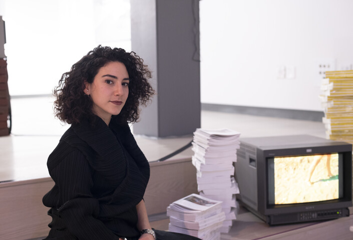 Argyro Nicolaou, seated next to a pile of books and an old tv set