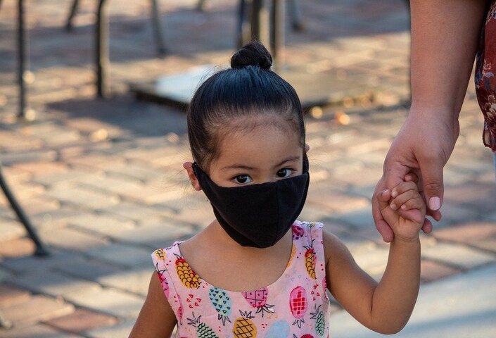 Young child wearing a mask, holding adult's hand