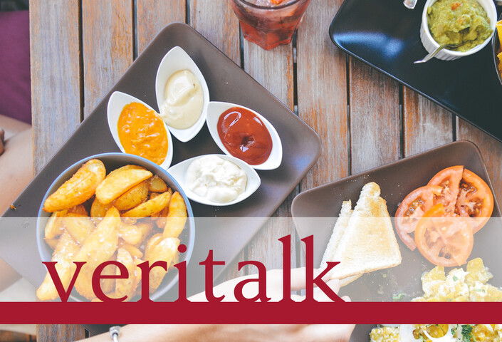 Veritalk logo over an image of a hand reaching for food on a wooden table - including bread, fries, dips, and a drink