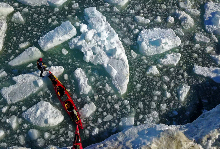 A team pulls red kayaks over ice and water