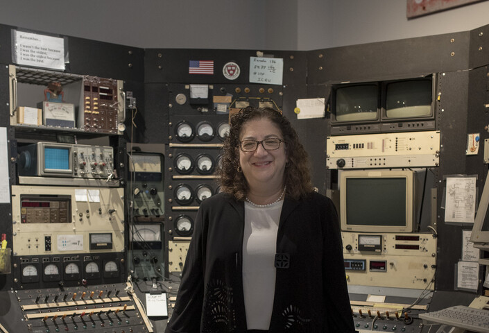 Sara Schechner poses next to the cyclotron control console