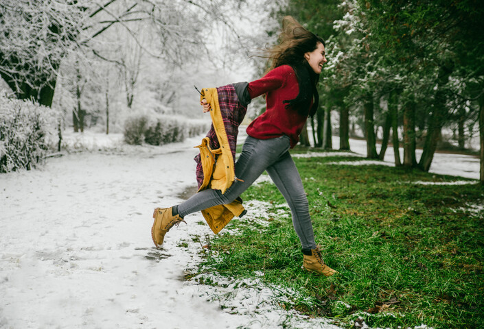 Woman jumping in snow onto grass