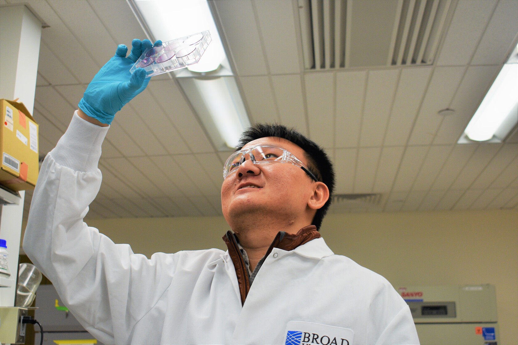 Liang Chang in lab holding a petri dish above his head