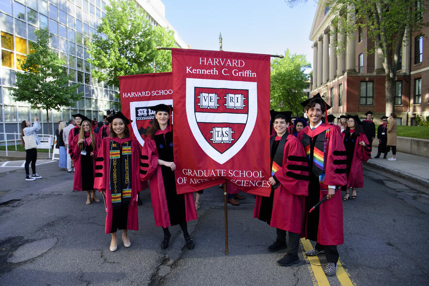 Students in commencement robes holding Harvard Griffin GSAS banner