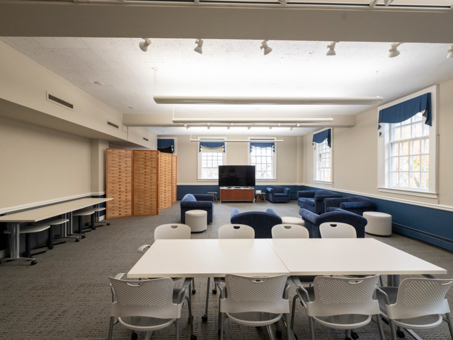 Large room with 2 white tables with chairs, a TV, and several couches