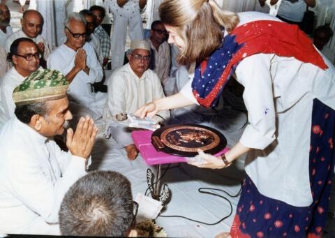 Diana Eck holding large medal surrounded by sitting people 