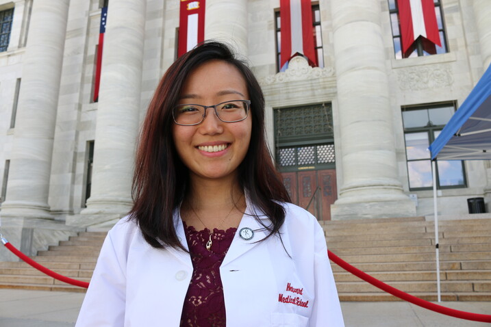 Wendy Sun smiling in front of Harvard Medical School in her white coat