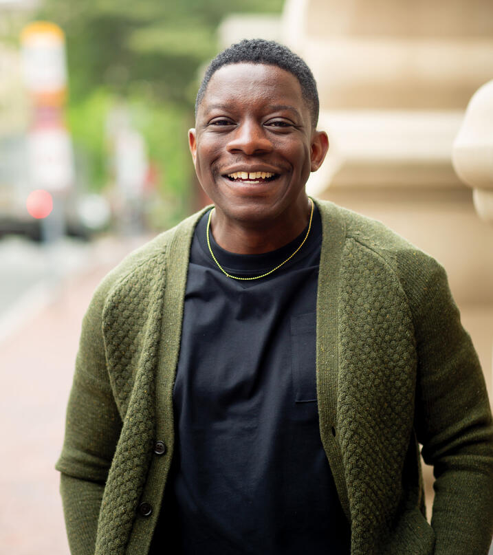 Adebanjo Adedoja smiling; wearing a black shirt with green sweater over it