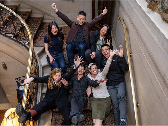 Group of people sitting on stairs smiling with hands in their air