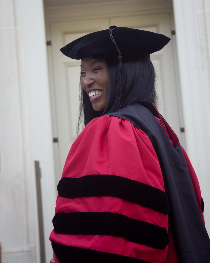 Anwulika smiling side profile wearing her Harvard GSAS regalia