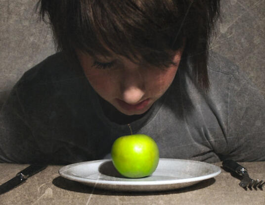 Child looking down at apple on plate
