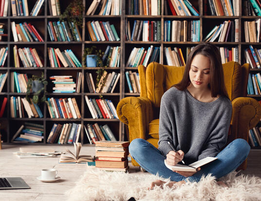 Woman sitting on floor with book in hand and bookshelves behind her