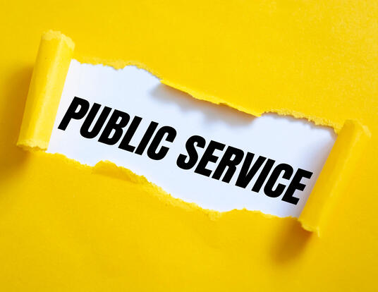 Public Service written in black and white being ripped open from yellow piece of paper
