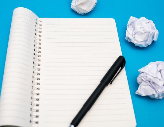 dissertation completion Notebook with pen and crumbled pieces of paper next to
