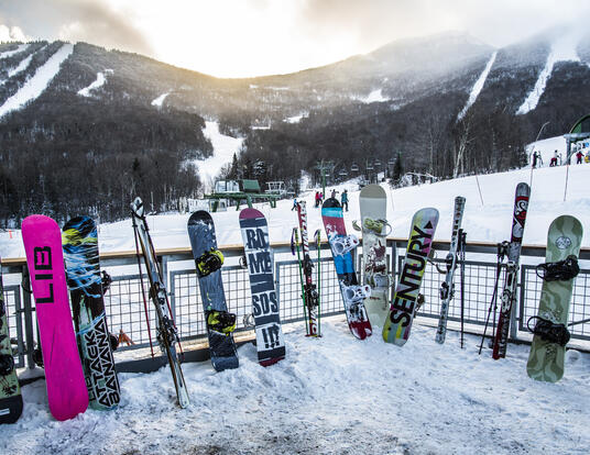 Shot of skis and snowboards leaning up against a fence looking up to Vermont's Jay Peak