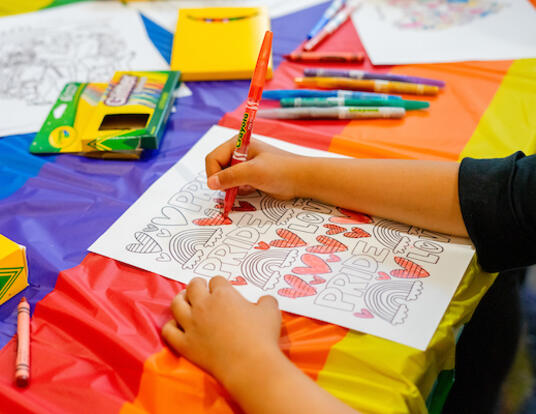 Child coloring in Pride Event picture with crayons surrounding