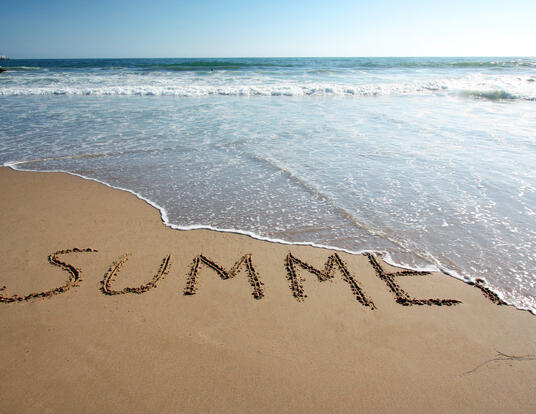 ocean tide washing away the word "Summer" written into the beach sand