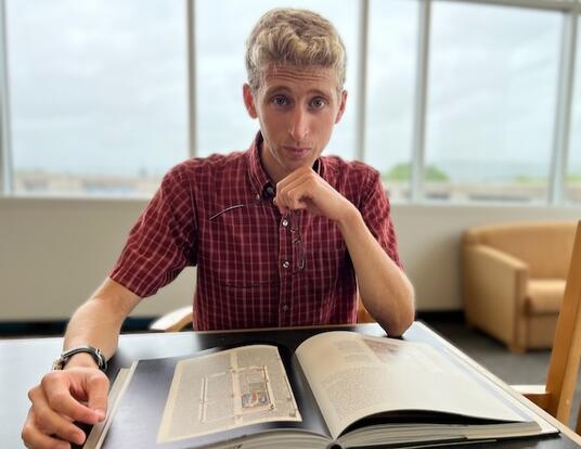 Headshot of Daniel Jacobs; hand on chin with book on desk