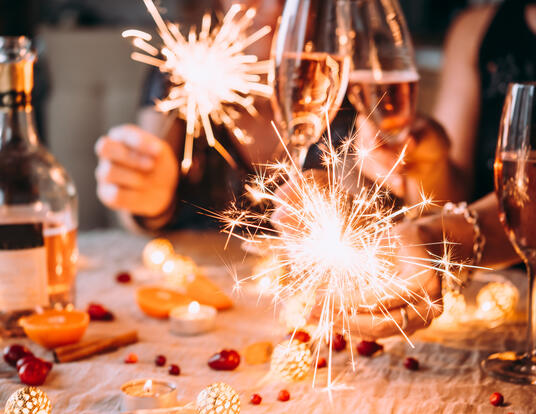 Upclose of people holding drinks and sparklers during the holidays