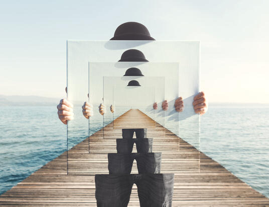 surreal image of man holding mirror depicting infinitely receding, mirrored versions of same image 