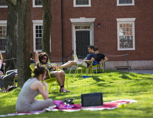 People sitting down on grass and in chairs in Harvard Yard