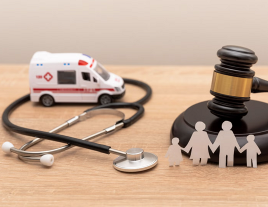Stock photo of miniature ambulance, stethoscope, and gavel on a wood tabletop