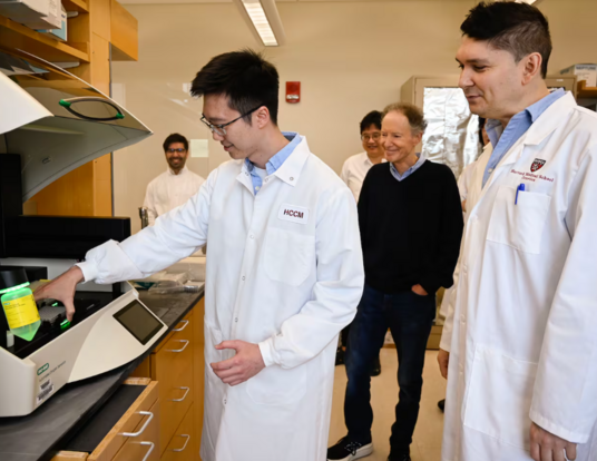 Dr. Bruce Yankner (center) watched as Zhen Kai Ngian (left) described the role of a digital droplet PCR machine used in the team's Alzheimer's research at the lab in the Harvard Medical research building.