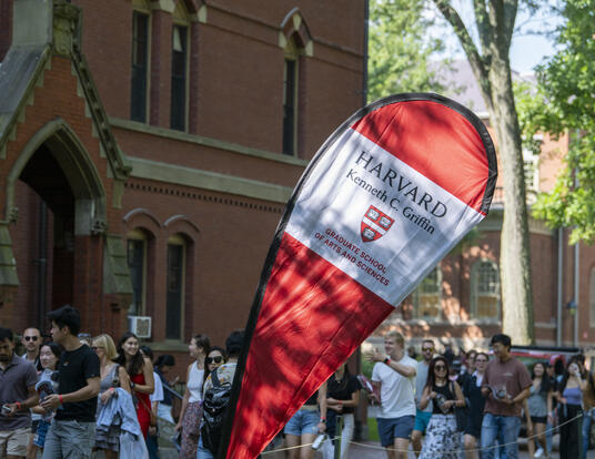 Harvard Griffin GSAS tear drop signage with students walking in background in Harvard Yard