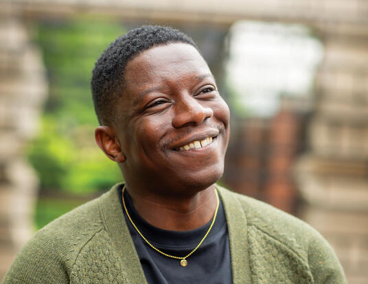 Adebanjo Adedoja smiling; wearing a black shirt with green sweater over it; holding hands