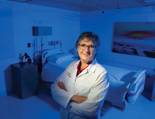Elizabeth Klerman in white lab coat with arms crossed with bed in back of her.