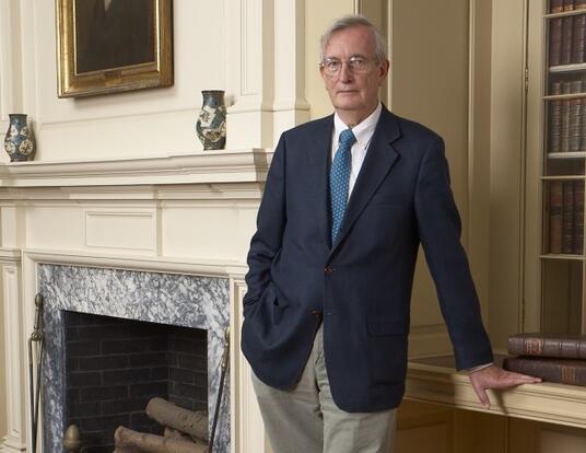 Dr. Keith Thompson standing to the right of a marble fireplace