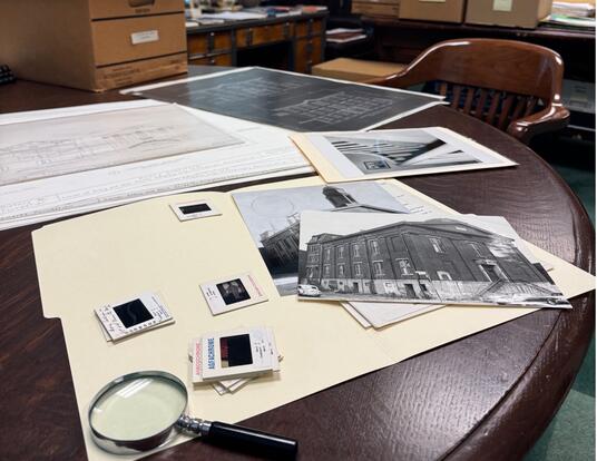 pile of photos and folders with magnifying glass on table