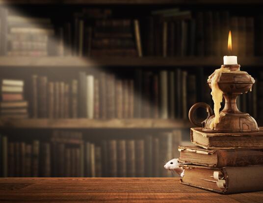 whimsical stack of books with candle melting on top and mouse peering out