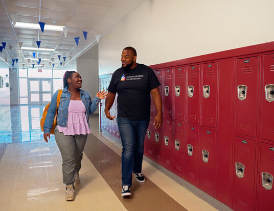 Black male wearing Communities in Schools shirt walking down the hall with a younger Black female